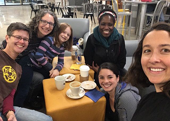 Five adults and a child sitting at a table with coffee cups smiling at camera.