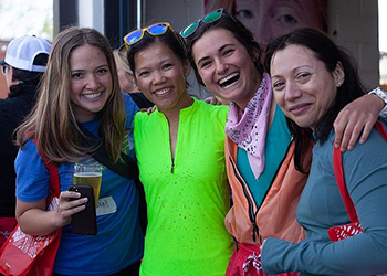 Four people looking directly at the camera smiling. One person is holding a beer.
